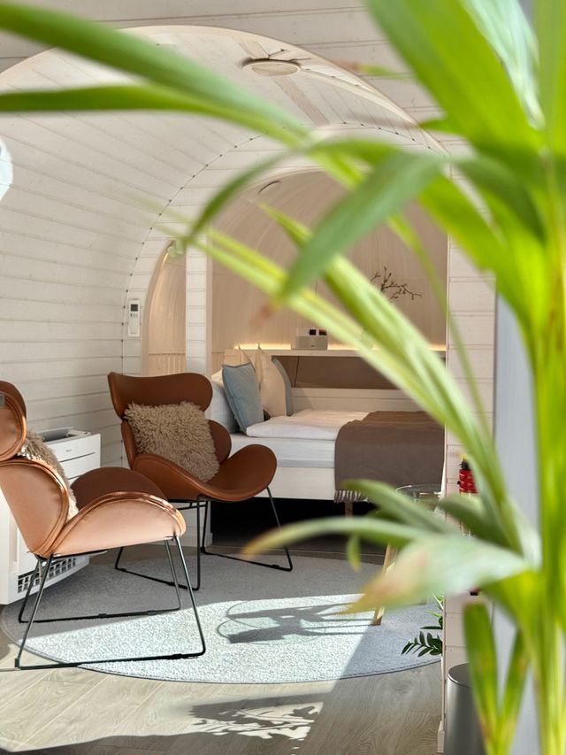 Lichtdurchfluteter Chalet-Wohn- und Schlafraum mit Sesseln und Blick durch grüne Pflanzen