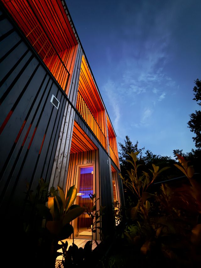 Beleuchtete Holzfassade der feinzeit Lofts in der Abenddämmerung