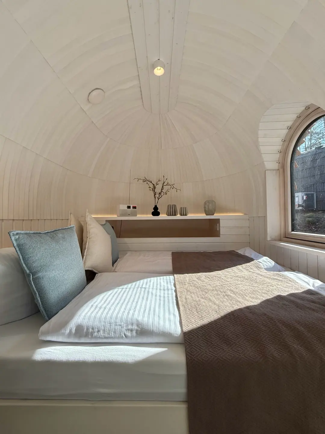 Bett unter der gewölbten Holzdecke eines Chalets mit Bogenfenster